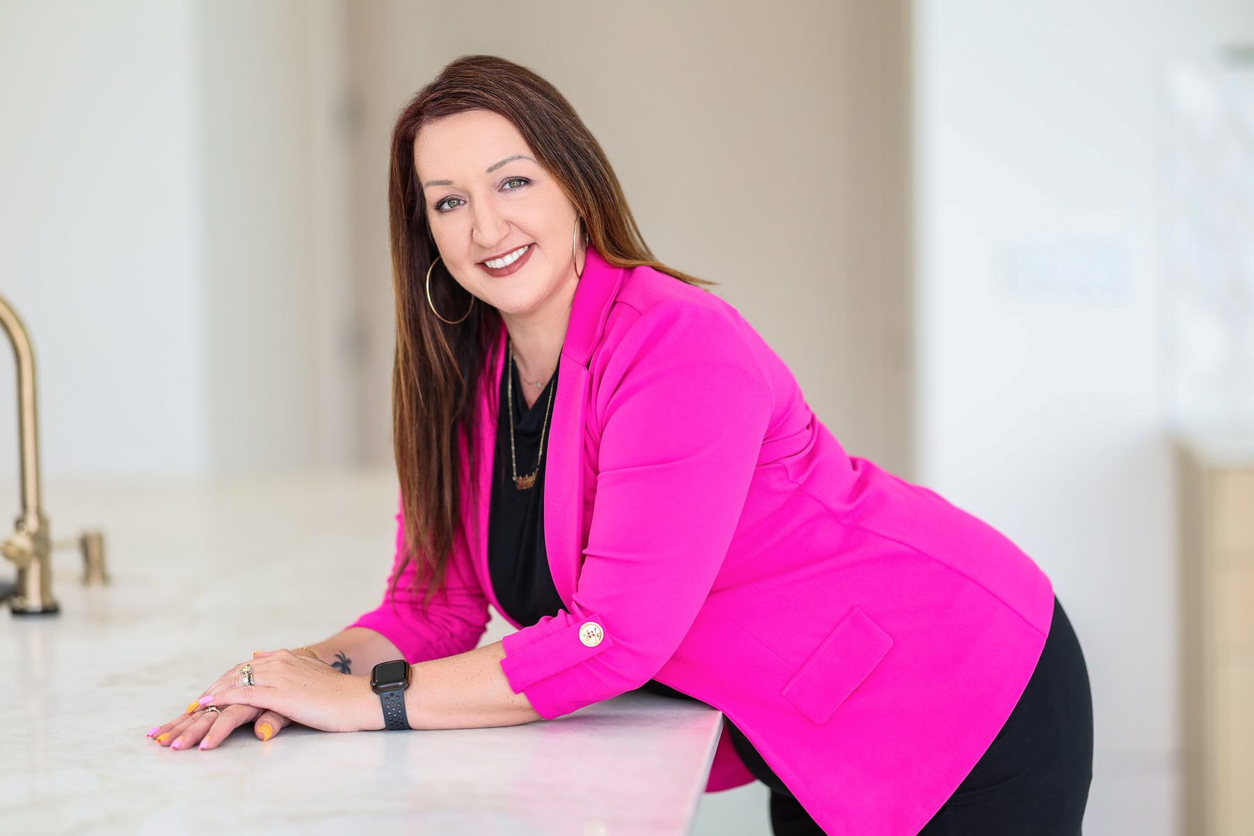 Stephanie Wilson in a hot pink blazer, leaning on a marble kitchen counter